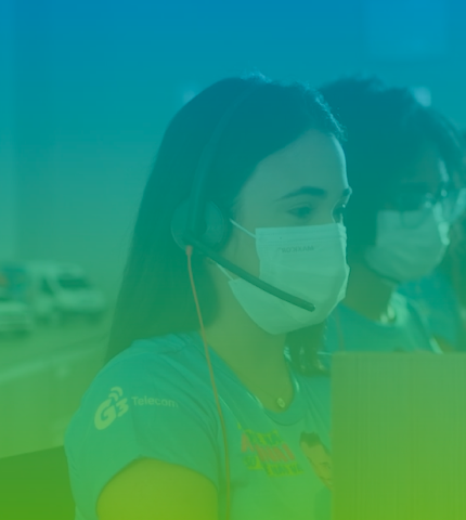 Banner da equipe de atendimento ao cliente da G3 Telecom. Atendentes uniformizados, usando máscaras de proteção e headsets, trabalham na central de call center para oferecer suporte e soluções aos clientes da empresa. Imagem com filtro verde e azul.